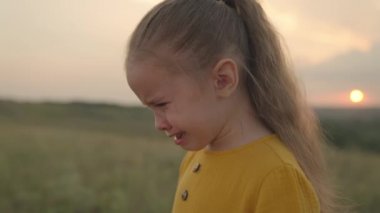 Küçük üzgün bir çocuk gün batımında ağlıyor, çocukların yüzünden gözyaşları akıyor, hoşnutsuz bir duygu ifadesi, ruhun stresi, kız itaat etmek istemiyor, çocuk problemi ıslak yüzü