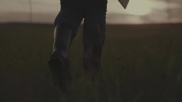 Boer in rubberen laarzen loopt over het veld met tablet in zijn hand, landbouw, zakenman in het veld bij zonsondergang, een agronomist loopt door een plantage van land, tijd om de grond te ploegen, 's avonds boerderij — Stockfoto