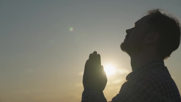 Ember imádkozik naplementekor, segítséget és támogatást kér az égtől, spirituális ember gondolkodik, a hit és a remény fogalma, tükröződik a napsugarakban, megbízható vallás — Stock videók