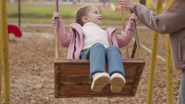 Criança balançando em um balanço e rindo enquanto voa para cima, um playground de outono, uma família feliz, uma mãe rola criança no parque da cidade, sonho de infância para voar, sorrir para a mãe em uma caminhada, brincar com um bebê — Fotografia de Stock