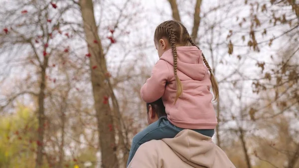 Niño se sienta su cuello padres, papá lleva niño en sus hombros en un parque de otoño, familia feliz, bebé monta padre amado, encantadora niña monta naturaleza al aire libre, paseo contra el fondo del cielo —  Fotos de Stock