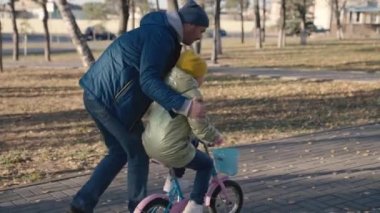 Neşeli baba iki tekerlekli bisiklete binmeyi öğretir mutlu aile, çocukluk hayali bisikletli çocuk baba neşeyle şehir parkı oynar bebek pedalları çevirir, kızıyla nişanlı ata biner