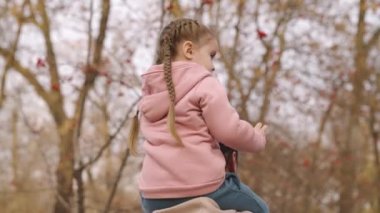 Çocuk babasının boynuna oturur, baba çocuğu sonbahar parkında omuzlarında taşır, mutlu bir aile, bebek gezintisi sevgili ebeveyn, büyüleyici küçük kız açık havada gezer, gökyüzünün arka planına doğru yol alır.