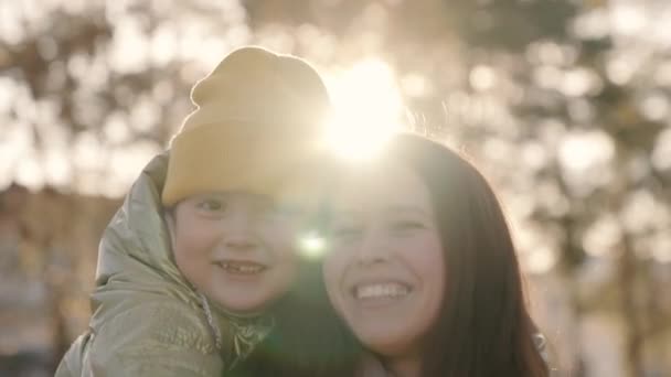 La madre y el niño se abrazan al atardecer del otoño en la ciudad, la familia feliz, la madre y el niño se ríen en sus brazos a la luz del sol, el padre alegre con la hija del bebé en reflejos brillantes, la vida de la niñez niña — Vídeos de Stock