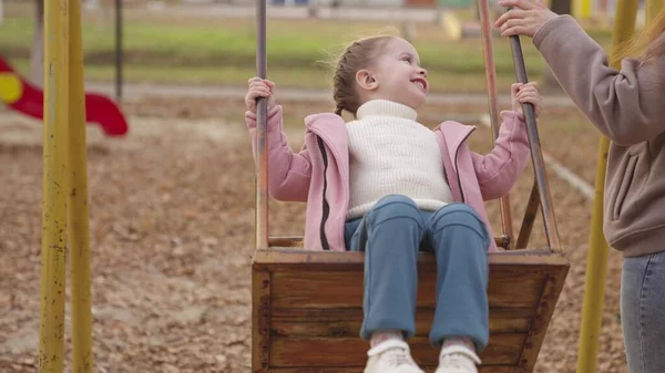 Criança balançando em um balanço e rindo enquanto voa para cima, um playground de outono, uma família feliz, uma mãe rola criança no parque da cidade, sonho de infância para voar, sorrir para a mãe em uma caminhada, brincar com um bebê — Fotografia de Stock