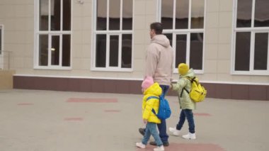 Baba, sırt çantalı çocukları okula, okul bahçesine, baba ve kızları sınıfa birlikte koşuyor. Mutlu aile, okuldan sonra çocuğu okula götürüyor, anaokulu eğitimi...