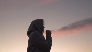 Pembe gökyüzü arka planında dua eden bir kız, iyiliğe inanır, yardım ister, rüya görür, motivasyon dışarıda ilham verir, kadın meditasyon yapmayı düşünür, seyahat tutkusu kavramı, ilahi ışık