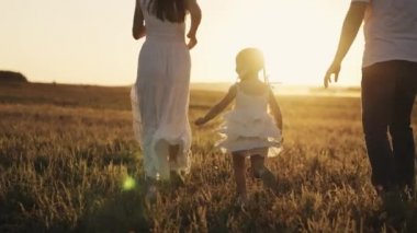 Küçük çocuk, gün batımında anne ve babasının elini tutuyor neşeli çocuk, anne ve babasına yetişmeye çalışıyor güneş ışığı parıldıyor, mutlu aile, bebek, şafak vakti parlayarak dışarı çıkıyor.