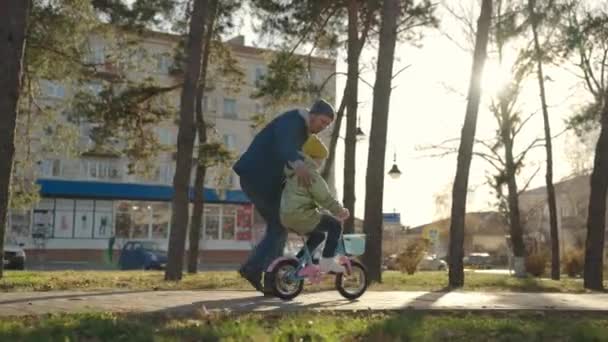 Babası neşeli küçük bir kıza bisiklet sürmeyi öğretiyor, mutlu bir aile, babası şehir parkında bir çocukla oynuyor, güneş ışığı altında, çocukluk hayali iki tekerlekli bisiklet sürmeyi öğrenmek.. — Stok video