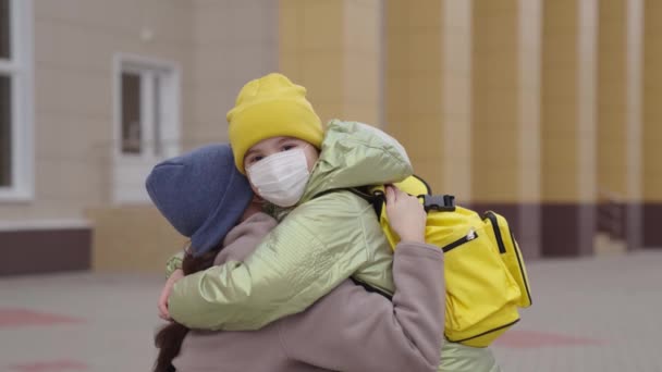 Abrazos del niño madre, madre escolta a su hija a la lección de la escuela, divertidas actividades de aprendizaje por placer, niño pequeño con mochila escolar cerca del edificio de la escuela, familia feliz, tiempo de aprendizaje de los niños — Vídeo de stock