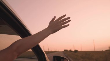 Özgür kız elini pembe bir günbatımında arabadan uzatıyor, yolda giderken eliyle rüzgarı yakalıyor, mutlu aile, rüya tatiline çıkıyor, yolculukta eğleniyor.
