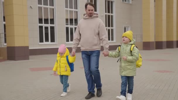 Otec vede malé děti se školními batohy základní školy, škola spěchu, dítě jít do třídy, zábavné vzdělávací aktivity baby school let života, táta s dívkami a dcerami ve městě — Stock video