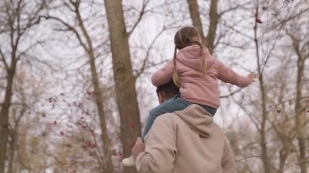 Niño pequeño se sienta sobre los hombros de su padre mientras camina en el parque de la ciudad, niño monta a su padre, feliz vida familiar, criar a una niña como un padre adulto, hija le encanta montar a su padre, hombre y bebé caminan juntos — Vídeos de Stock