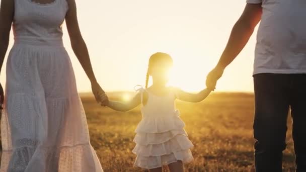 Holčička dcera vede ruku otce a matky při západu slunce, šťastný rodinný život, veselí lidé s dětmi procházka v parku, muž žena a dítě cestování na dovolenou ve světle slunečního světla — Stock video
