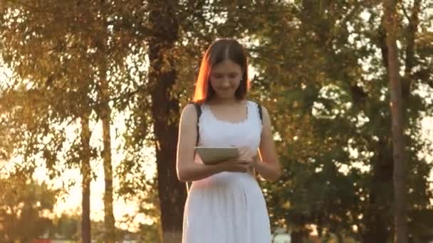 Egy lány tanul egy táblagépen a város napsugaraiban, napnyugtakor online vásárol egy online boltban, megnézi a leveleket a közösségi oldalakon, csevegnek, könyveket olvas és híreket az oldalak információs forrásaiban — Stock videók