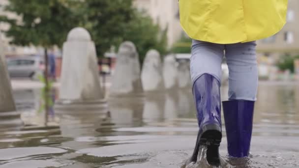 Człowiek idzie przez głęboką kałużę w gumowych butach, woda pluska latać w różnych kierunkach, deszcz spadł z nieba, powódź w mieście, chodzić ulicą z nogami — Wideo stockowe