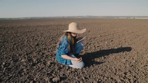 畑でタブレットを使って畑で作業する農家春の土に苗を植える準備をする農家農村の土地にガジェットのある帽子の農学者ビジネス女性 — ストック動画