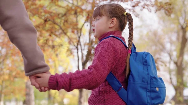 Un niño con una mochila escolar está sosteniendo la mano de una madre que va a la escuela, una hija con su madre se apresura a las clases escolares en el aula, educación divertida para los niños, una familia feliz — Foto de Stock