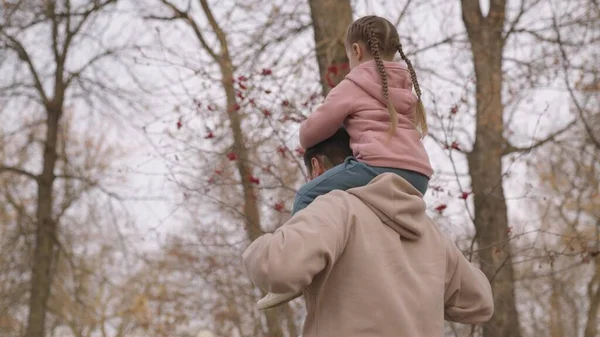 Petit enfant s'assoit sur les épaules de son père tout en marchant dans le parc de la ville, enfant chevauche son père, vie familiale heureuse, élever la fille comme un parent adulte, fille aime monter son père, homme et bébé marchent ensemble — Photo