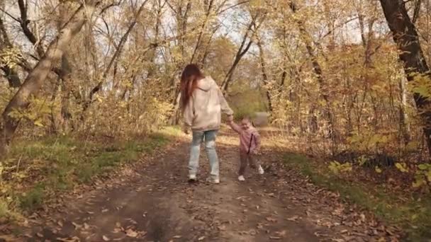 Kind rennt um seine Mutter und lacht im Park, glückliche Familie, fröhliches Kind mit Mama spielt ein Spiel, goldener Herbst mit schönen abgefallenen Blättern im Wald, kleines Mädchen lächelt beim Spaziergang und springt — Stockvideo