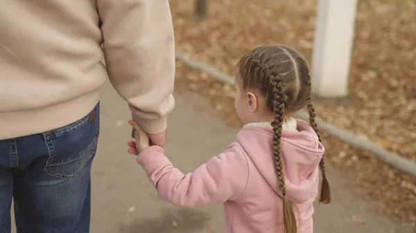 Malá holčička drží svého otce za ruku, dítě prochází podzimním parkem, šťastný rodinný život, dcery den volna s tatínkem, procházky po silnici ve městě, Den otců, opatrovnictví a výchova dítěte — Stock fotografie