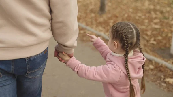 小さな子供の女の子は父親の手を取り、子供は秋の公園を歩き、幸せな家族生活、パパとの娘の日、街を歩く、父の日、赤ちゃんの親権と養育 — ストック写真