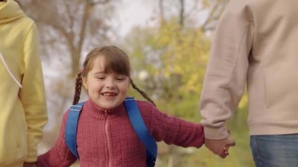 Menina criança feliz corre com sua mãe e pai no parque da cidade, vida familiar feliz, criança alegre com mochila corre para a escola no pátio da escola, tempo para estudar e obter uma educação, filha com os pais — Vídeo de Stock