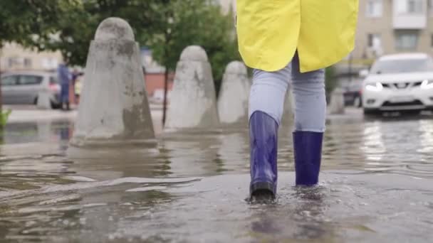 Un hombre camina a través de un charco profundo en botas de goma, salpicaduras de agua vuelan en diferentes direcciones, la lluvia ha caído del cielo, una inundación en la ciudad, caminar por la calle con los pies — Vídeos de Stock