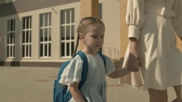 Mère conduit un petit enfant par la main à la première année de l'école primaire, sac d'école sur les épaules d'une fille, famille heureuse, se précipiter à la leçon dans la cour d'école, enfant avec sac à dos recevra une éducation — Video