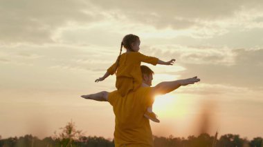 çocuk babasının omuzlarında oturur gün batımında uçmayı hayal eder, güneşin parıltısı pilot olmak ister, babasıyla birlikte oynamak ister, bebek doğada ebeveyniyle oynar, mutlu bir aile, seyahat
