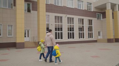 Küçük kızlar babalarını sırt çantasıyla şehir sokaklarında okula giderken tutarlar, çocuklar eğitim alırlar, mutlu bir aile hayatı yaşarlar, baba okul çantasıyla komik çocuğu birinci sınıfa götürür.