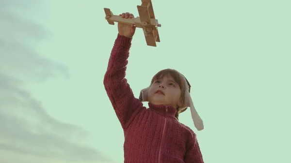 Pequena criança em um capacete brinca com um avião contra o céu, sonho de infância para voar, criança quer se tornar um piloto de avião, imaginação, família feliz, bebê alegre faz voo ilusão em fantasias — Fotografia de Stock