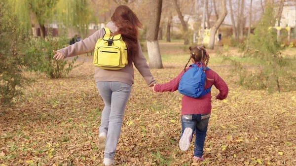 Cheerful mother and child run with backpacks their shoulders autumn park, happy family life, run school for lessons, education knowledge time, achieve success, sports trip around city, active mother — Stock Photo, Image