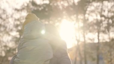Çocuk güneşin ışığında neşeli anneye sarılıyor, mutlu aile hayatı, küçük çocuk gün batımında annesiyle birlikte şehir parkında dönüyor, çocuksu ruh halinin kahkahaları ve neşesi, sevgili annesiyle kız çocuğu, oyun oynuyor.