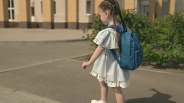 Sırt çantalı küçük bir kız okul bahçesinde okula gidiyor, ilkokul çocukları için eğitim programı kaldırımda yürüyor ve eğleniyor, çocukluk hayalleri kurarak yeni bir hayat kuruyor.