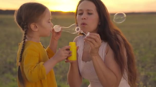 Bambino che soffia bolle di sapone con la madre al tramonto, felice vita familiare, bambina con la mamma gioco con il sapone nella natura, palle divertenti, week-end attivi congiunti con la ragazza, parco a piedi sera — Video Stock