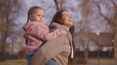 Çocuk annesine boynundan sarılıyor ve gülüyorlar. Annesi kucağına alıyor ve gülümsüyor. Mutlu aile hayatı, neşeli küçük kız çocuğu annesini sırtında taşıyor.