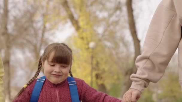 Lycklig liten flicka kör med sin mor och far i stadsparken, lycklig familjeliv, glada barn med ryggsäck rusar till skolan i skolgården, tid att studera och få en utbildning, dotter med föräldrar — Stockvideo