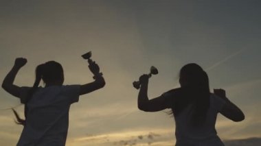 Elinde fincanı olan bir kızın silueti zaferle sevinir, mutlulukla zıplar, altın kazanarak, aktif rekabet kazanarak ve ödül alarak başarı elde eder, takım çalışmasında güler ve kucaklaşır, sporda gülümser.