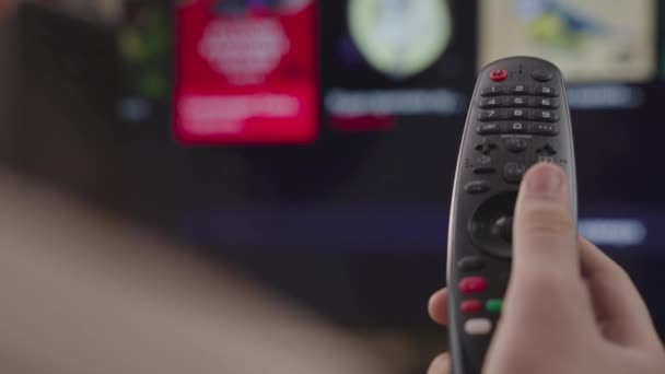 Ragazza controlla il telecomando della TV in camera a casa, riposo nel fine settimana, telecomando di una moderna smart TV, controllo TV e canali cinematografici, primo piano, schermo sfocato, dispositivo di scorrimento pagina intelligente — Video Stock