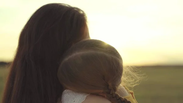 Pequeño niño abraza a la madre en los rayos del sol, familia feliz al atardecer, la mujer ama al niño, toma la maternidad un sentimiento agradable, niña hija con mamá en un viaje contra el cielo, custodia del bebé — Foto de Stock