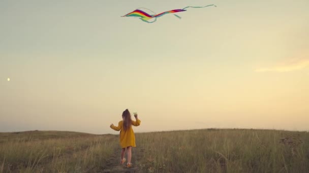 Little girl runs along the road catching wind in a kite at sunset in sky, childhood dream of flying, happy family, child plays color game in nature, joyful kid is fun, colorful baby fantasy in glare — Stock Video