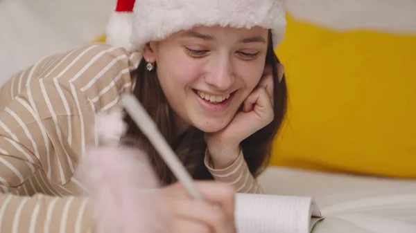 Noel Baba şapkalı bir kız Noel dileği yazar, yeni yıl tatili, çocukluk hayalleri, mutlu bir ergenden tebrik mektubu, bir şenlik mucizesi bekler, yılın sürprizini bekler.
