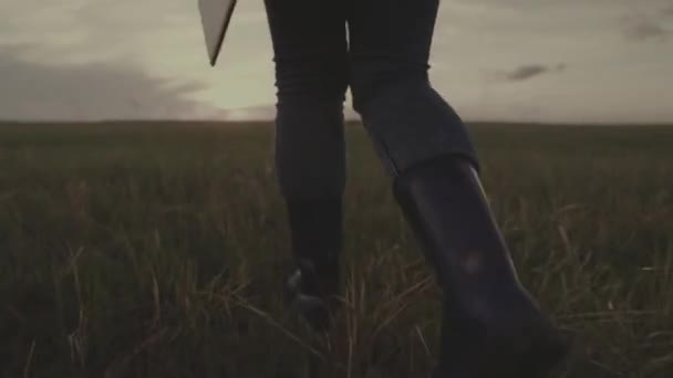 Farmer in rubber boots walks across the field with tablet in his hand, farming, business man in field at sunset, an agronomist walks through a plantation of land, time to plow the soil, evening farm — Stock Video