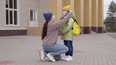 Bir anne, okul saatlerinde küçük bir çocuğu korumak için yüzüne tıbbi maske takar. Annesi sırt çantalı çocuğa sarılır. Koronavirüs enfeksiyonundan korunur.