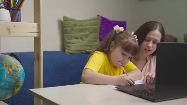 little child writes homework with a pen in a notebook, a kid does homework with his mother at home, modern baby distance learning, preschool education with a computer, childrens home knowledge desk