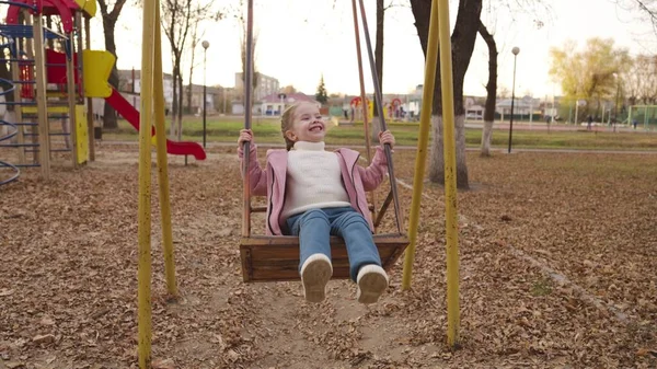 Uma criança alegre balançando em um balanço em um parque de outono, uma família feliz, uma criança voa alto no ar, jogando um jogo ao ar livre no playground, bebê menina caminha no parque e sorri, alegria das crianças — Fotografia de Stock