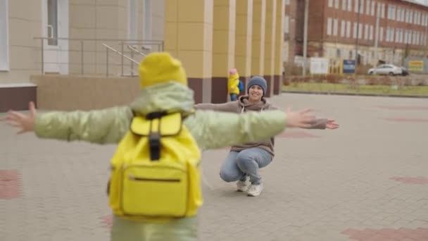 Mother greets little child from school with hug, a kid with school backpack runs to his mother, happy family life, motherly care for her daughter, schoolgirl of an elementary educational institution — Stock Video