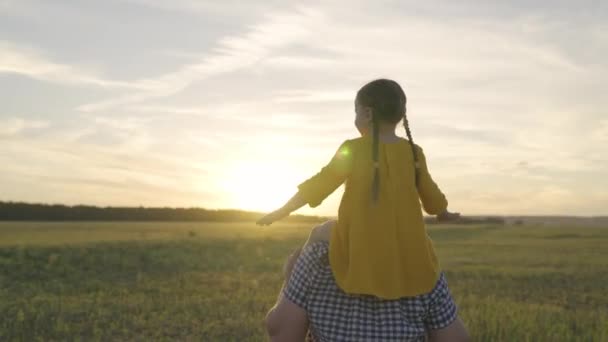 Criança senta-se nos ombros de seus pais, correndo ao pôr do sol, família feliz, criança pequena com sonhos do pai se tornando um piloto à luz dos raios de sóis, entretenimento divertido do sonho da infância, menina levantou as mãos — Vídeo de Stock