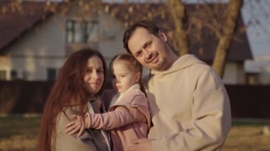 Küçük kız çocuğu annesinin kollarında oturuyor, mutlu aile, gülen insanlar, evin arka planında baba anne ve çocuk portresi, çocuklu genç bir çiftin yeni evine taşınıyor.